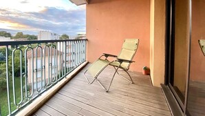 Un balcone con pavimento in legno, ringhiera in metallo e una singola sedia pieghevole verde.