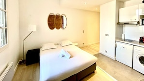 Habitación de hotel moderna con una cama grande, una lámpara de noche, un espejo en la pared y una kitchenette con microondas y lavadora.