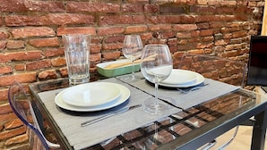 Una mesa servida con dos platos, dos copas de vino y un vaso de agua, frente a una pared de ladrillo.