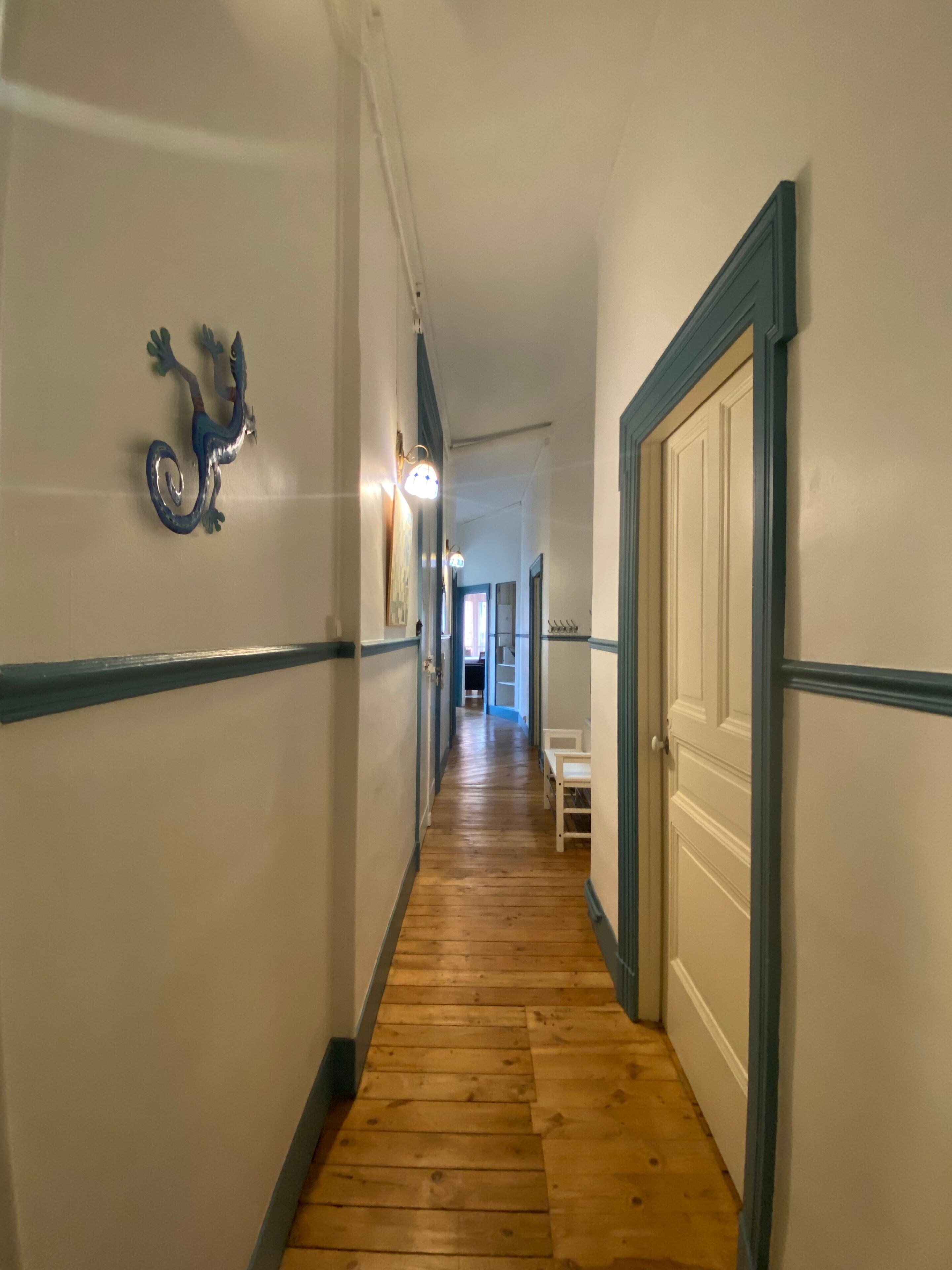 A hallway with wooden flooring, white walls, and blue trim. There is a door on the right and a wall-mounted decoration on the left.