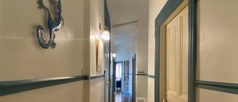 A hallway with wooden flooring, white walls, and blue trim. There is a door on the right and a wall-mounted decoration on the left.