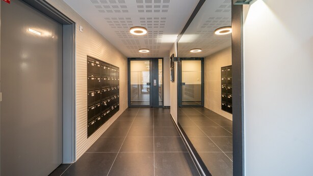A modern hallway with lockers, recessed lighting, and a view into a room. - Carré d’As - Appartement de standing (Le Bourget)
