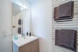 A bathroom with a white sink, mirror, and towel rack. - Carré d’As - Appartement de standing (Le Bourget)