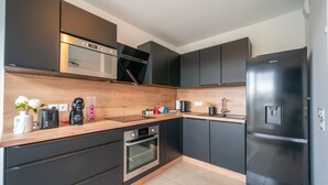 A modern kitchen with dark cabinetry, a wooden countertop, a built-in oven, a microwave, and a stainless steel refrigerator. - Carré d’As - Appartement de standing (Le Bourget)