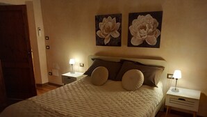 A neatly made bed with a quilted cover, two wall-mounted lamps, and two large floral paintings above the bed. - Clery house, a stone's throw from Florence, Tuscan style (Montelupo Fiorentino)