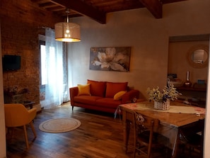 Ein gemütliches Wohnzimmer mit Holzboden, einem roten Sofa, einem Esstisch und einer Hängeleuchte.