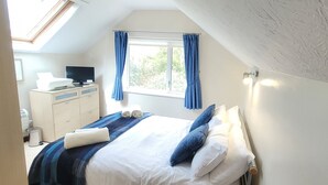 A bedroom with a bed, a desk with a computer, a window with curtains, and a skylight. - Birchcroft Hideaway (Ferndown)