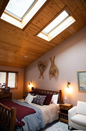A bedroom with a wooden ceiling, skylights, a bed with multiple pillows, a nightstand, a chair, and wall-mounted lights. - Whitefish 3 Bdrm, near ski&town w/views & hot tub (whitefish)