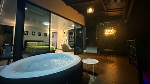 Een moderne hotelkamer met een ruime jacuzzi, een glazen wand en een neonbord.