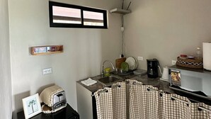 Een kleine keuken met een koelkast, een spoelbak, een raam en een koffiezetapparaat.