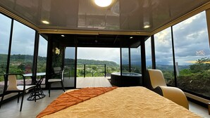 Een ruime kamer met een groot bed, een zithoek met stoelen en een whirlpool. De kamer heeft grote ramen met uitzicht op het landschap.