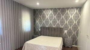 A bedroom with a bed, a nightstand, a lamp, and a wall with patterned wallpaper. - Moradia Privada COM Piscina Perto DA Praia (Apúlia)
