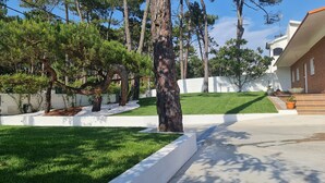 A residential area with a well-maintained lawn, a white wall, and a variety of trees. - Moradia Privada COM Piscina Perto DA Praia (Apúlia)