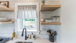 A kitchen with a window, a sink, and shelves with kitchenware.