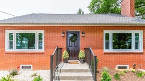 A two-story brick house with a front porch, a dark front door, and a wreath above it.