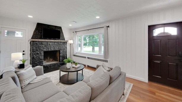 A living room with a stone fireplace, a sofa, a coffee table, and a window with curtains.