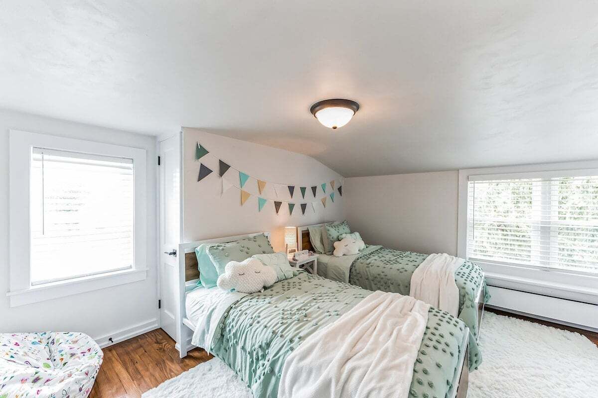 Ein Schlafzimmer mit zwei Betten, einer weißen Wand, einem Fenster und einer Deckenleuchte.
