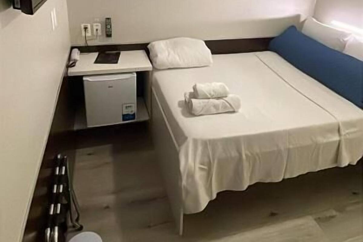Una habitación pequeña y limpia con una cama, un escritorio y un televisor.