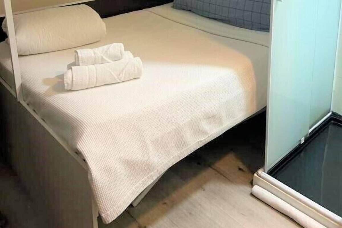 Dormitorio con literas, cabecera blanca, mesita de noche y una ventana pequeña.