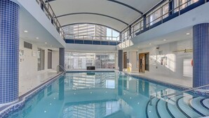 Una amplia piscina interior con techo curvo y un balcón en un segundo nivel.