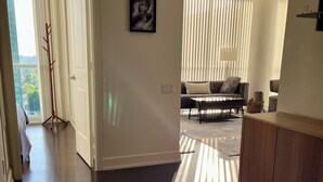 Una sala moderna con un sofá, una mesa de centro y una lámpara. Se observa un mueble de madera y un cuadro en la pared.