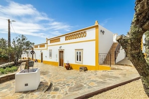 Um edifício branco com detalhes amarelos e um pátio pavimentado em pedra.