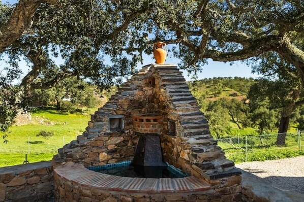 A stone structure with a chimney, a wooden bench, and a large pot on top.