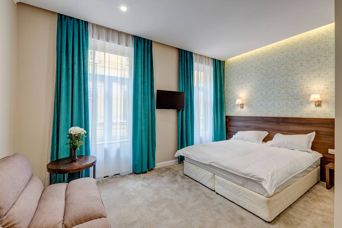 A hotel room with a large bed, a TV mounted on the wall, a small table with a vase of flowers, and a sofa.