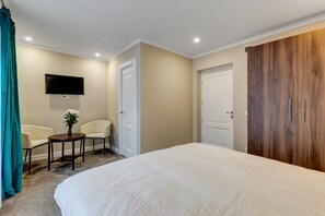 A bedroom with a large bed, a TV mounted on the wall, a chair, a small table with a vase, and a wardrobe. - UPSTAIRS BOUTIQUE (Bucharest)