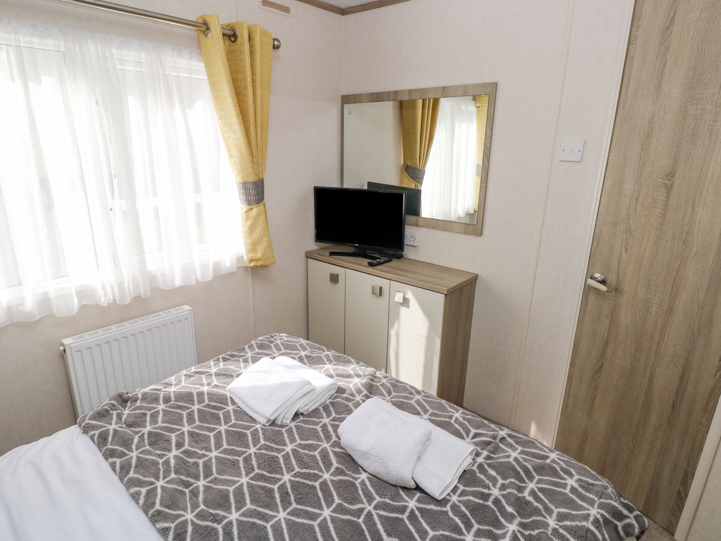 Een slaapkamer met een bed, een televisie op een meubel, een spiegel en een deur.