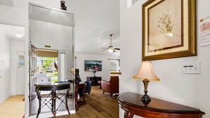 Un intérieur avec un plancher en bois, une table à manger, une lampe, un tableau encadré et un ventilateur de plafond.