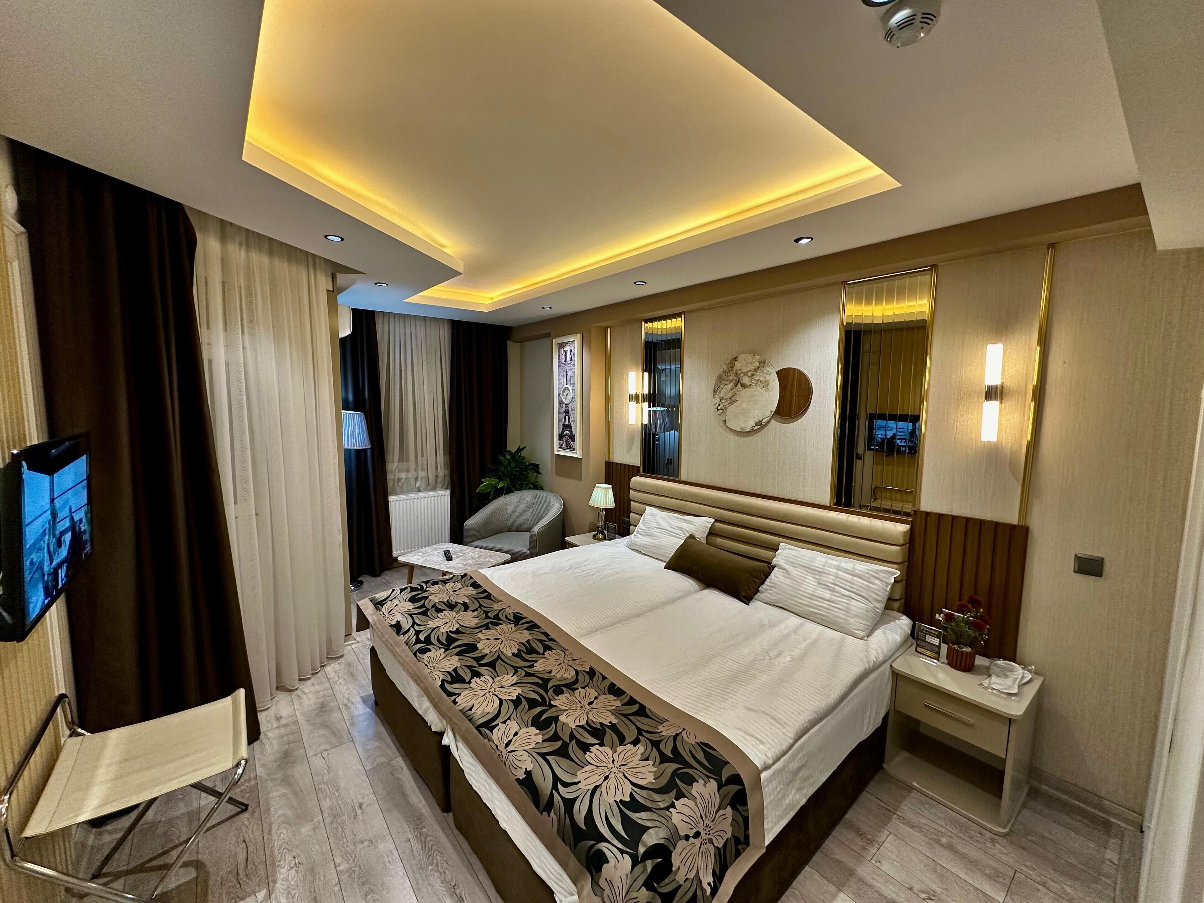 A modern hotel room with a large bed, bedside tables, a TV, and a desk.