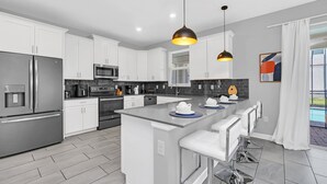 A modern kitchen with white cabinets, stainless steel appliances, a central island with bar stools, pendant lighting, and a view of a pool.