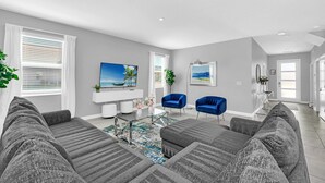 A modern living room with a gray sectional sofa, two blue armchairs, a coffee table, and a flat-screen TV.