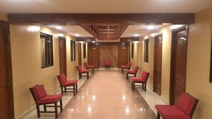 Un couloir d’hôtel avec des chaises rouges et des portes en bois, portant les numéros 115, 118, 119 et 120.