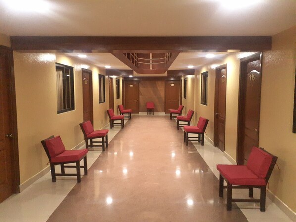 A hotel hallway with red chairs and wooden doors, numbered 115, 118, 119, and 120.