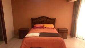 Un lit bien fait, avec une tête de lit en bois, deux tables de chevet et une fenêtre avec des rideaux.