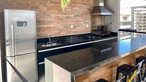 A modern kitchen with a stainless steel refrigerator, a black countertop, and a hanging fern. - AP 1422 com Piscina, Academia e Coworking (Juiz de Fora)
