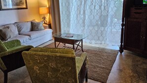 A living room with a sofa, a green armchair, a glass coffee table, and a patterned rug. - Magens Bay 3 minutes drive to Rustic Cabin 
 (St Thomas)