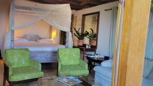 A bedroom with a canopy bed, two green patterned armchairs, a small table with a magazine, and a mirror on the wall. - Magens Bay 3 minutes drive to Rustic Cabin 
 (St Thomas)