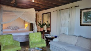 A bedroom with a bed, green chairs, a sofa, a nightstand, and a bedside table with lamps and a plant. - Magens Bay 3 minutes drive to Rustic Cabin 
 (St Thomas)