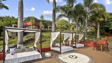 A tropical outdoor area with four canopy beds, a round table, and chairs.