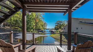 Una terraza de madera con dos sillas Adirondack, con vista a un cuerpo de agua y un puente.