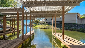 Una terraza de madera sobre una masa de agua con una estructura de techo metálico.