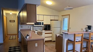 Una cocina compacta con armarios de madera, microondas, estufa y refrigerador. Hay una pequeña isla con taburetes y una cafetera.