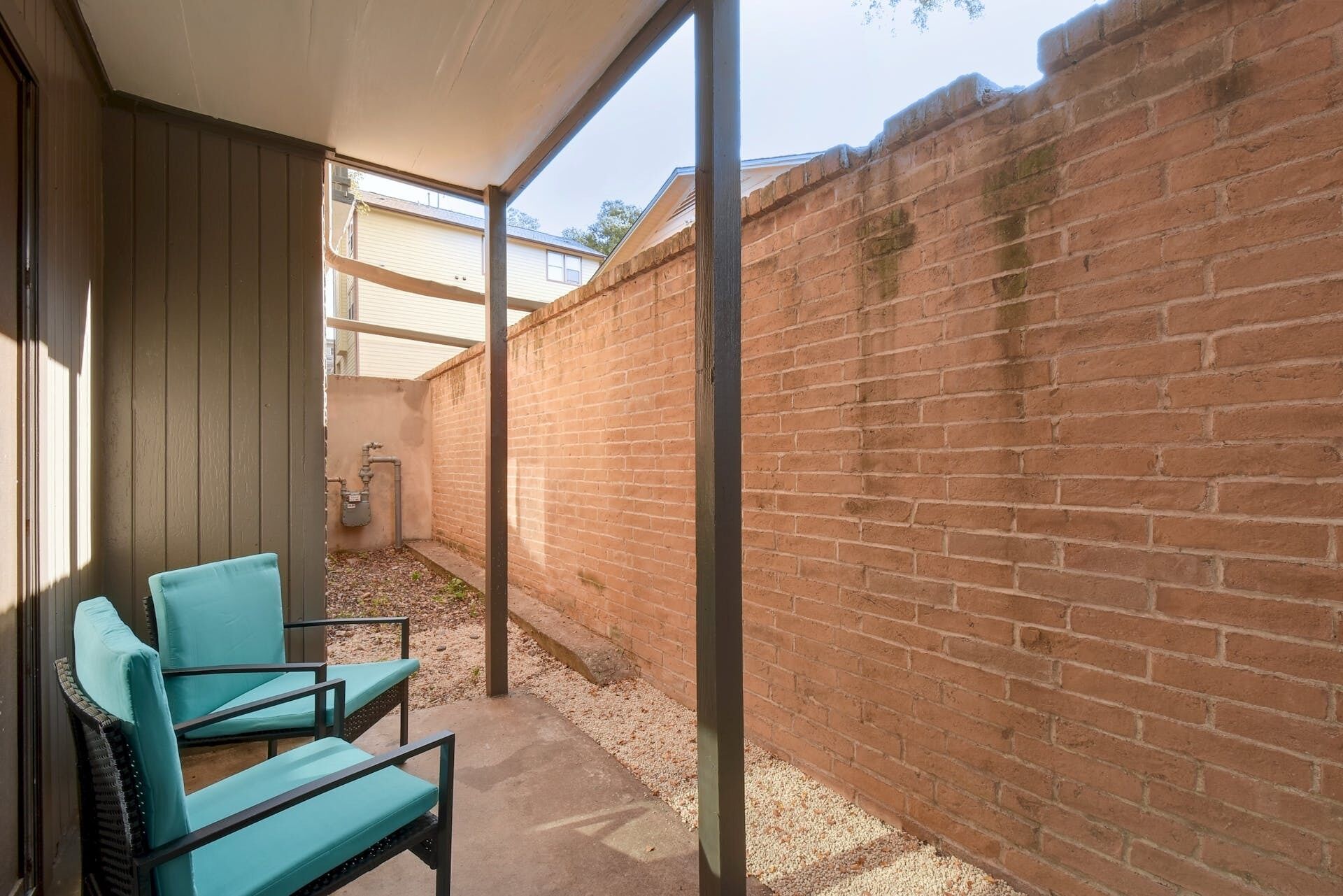A covered outdoor area with a brick wall, a concrete floor, and two turquoise chairs.
