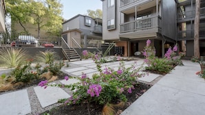 A modern multi-story building with balconies and a landscaped courtyard featuring purple flowers. - 30+ Days - North UT Apt 12 - 1 mi Moody Center (Austin)