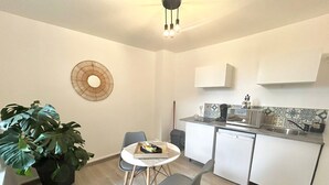 Une cuisine compacte avec un coin repas, comprenant une table ronde, deux chaises, une plante en pot et un luminaire moderne.