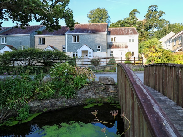 A residential area with houses, a wooden bridge, and a small pond with aquatic plants. - Primrose Cottage (Falmouth)