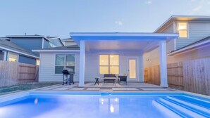 En lukket baghave med swimmingpool, overdækket terrasse med bord og stole, og et træhegn.
